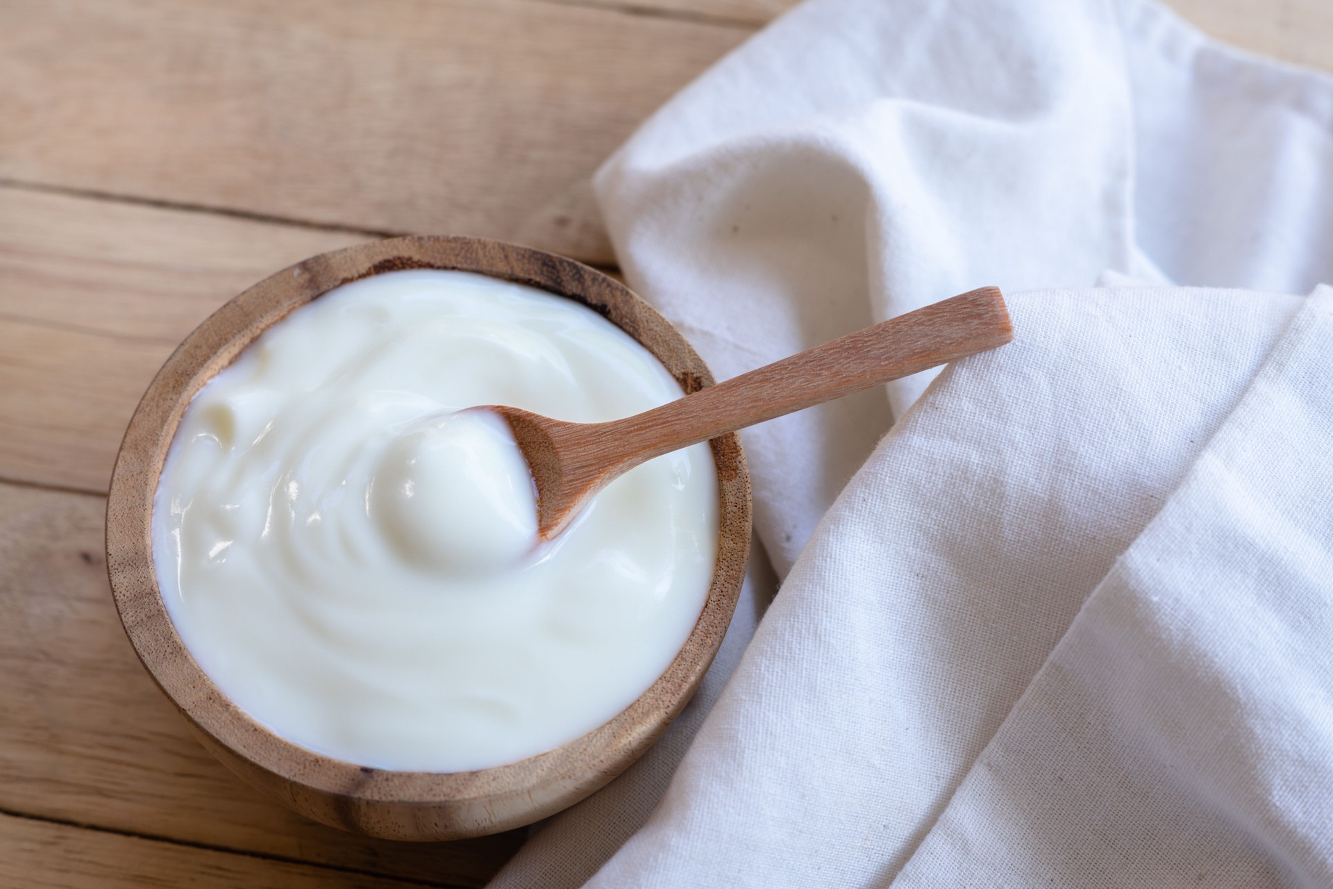 Yogur orgánico natural casero en tazón de madera y cuchara de madera sobre fondo de textura de madera, espacio de copia