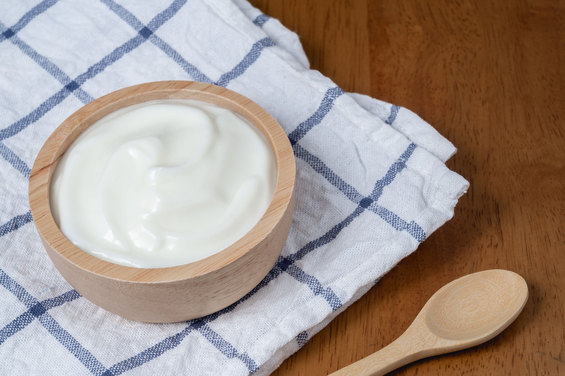 Yogur orgánico natural casero en tazón de madera y cuchara de madera sobre fondo de textura de madera, espacio de copia