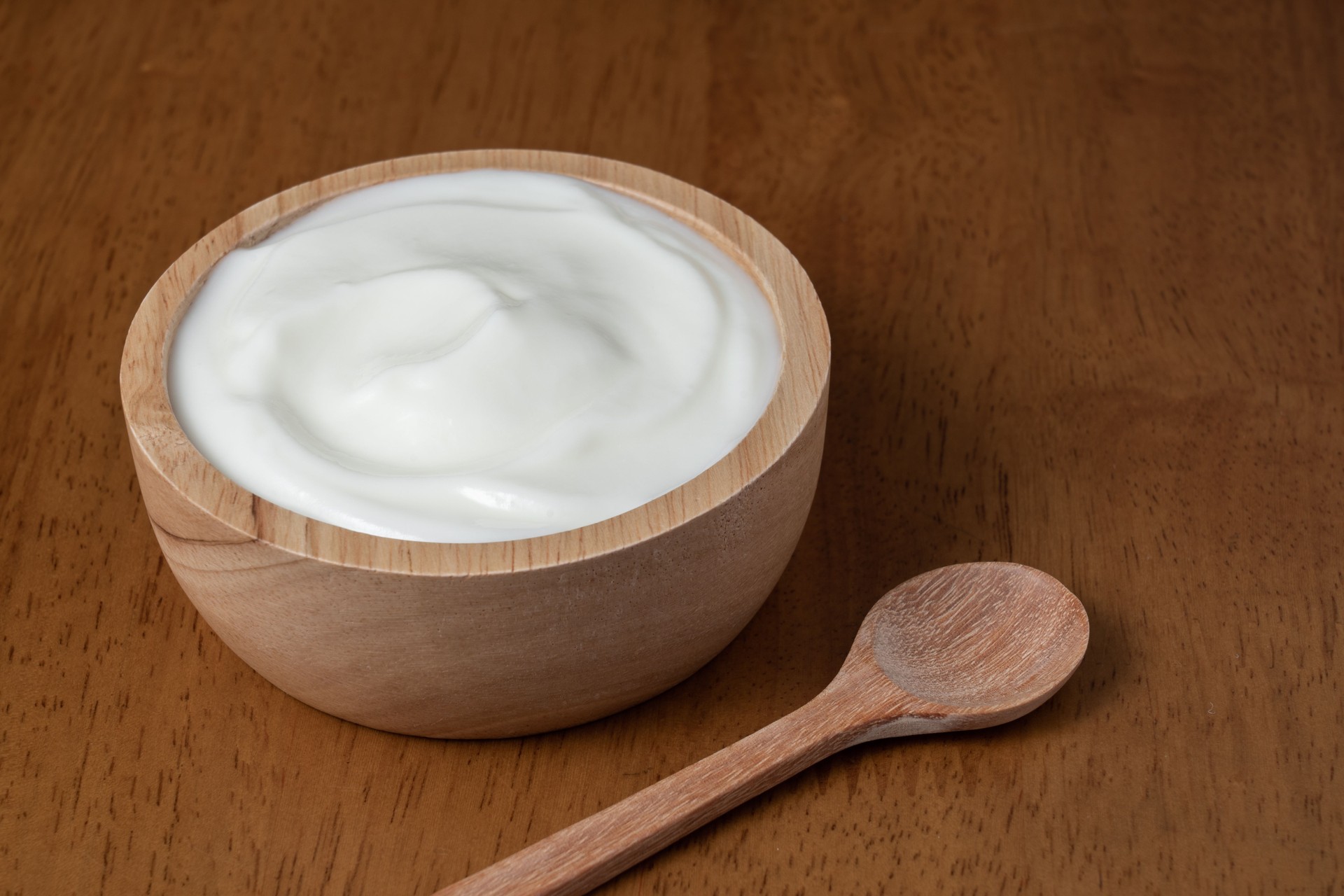 Yogur orgánico natural casero en tazón de madera y cuchara de madera sobre fondo de textura de madera, espacio de copia