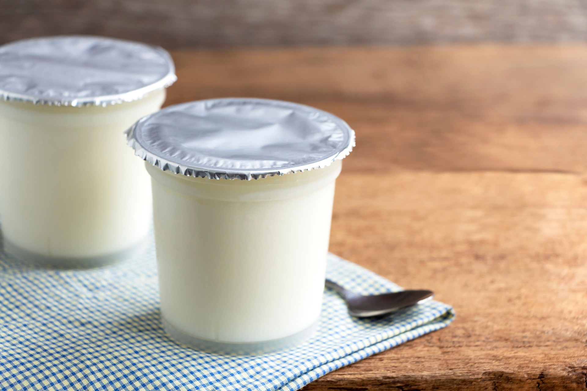 A breakfast of yogurt with a spoon placed on a wooden table. Yogurt made from milk fermented by added bacteria, often sweetened and flavored.